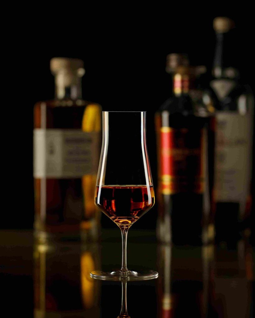 Copa Zalto Denk'Art Cask con whisky y botellas al fondo